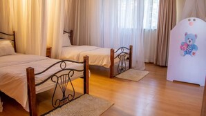 Une chambre avec deux lits, un plancher en bois et des rideaux légers.