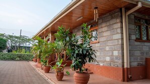 Un bâtiment doté d’un toit en bois et de murs en pierre, avec de grands pots de plantes placés devant l’entrée.