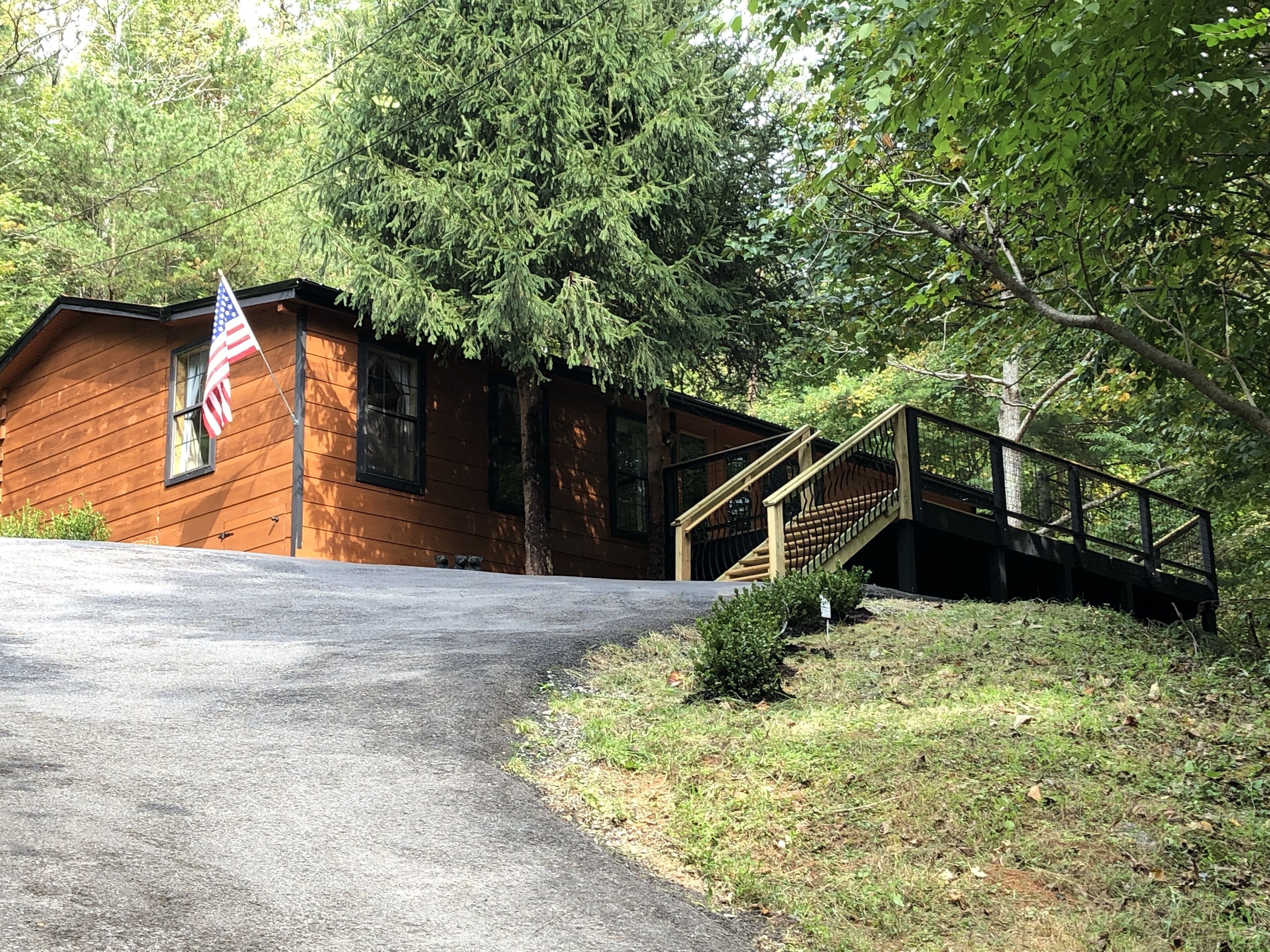 A wooden cabin with a flag, a staircase, and a paved driveway.