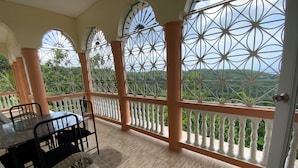 Un balcon avec une table et des chaises, un canapé et une vue sur la verdure.