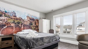 Ein Schlafzimmer mit einem großen Bett, einem Kleiderschrank, einem Sessel und einem Fenster mit Jalousien.