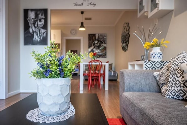A modern living room with a grey sofa, a patterned throw pillow, and a potted plant on a wooden table.