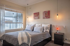 A bedroom with a bed, bedside table, and a window with blinds. - Seaside Escape @ Irene's Seaside Villa. 2br✔Nespresso✔Netflix✔Kitchen✔Carpark (Somerton Park)