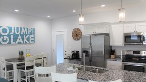 Une cuisine moderne avec des meubles blancs, des comptoirs en granit, des appareils électroménagers en acier inoxydable et un coin repas avec des chaises et une table blanches.