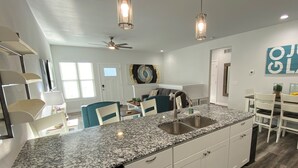 Une cuisine moderne dotée de plans de travail en granit, de meubles blancs et de luminaires suspendus.