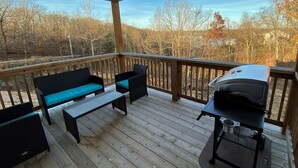 Une terrasse couverte avec un barbecue, un espace salon et une vue sur les arbres.