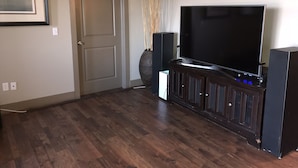 A living room with a large flat-screen TV, dark wood flooring, a door, and a framed picture on the wall. - Luxury Condo downtown Lansing (Lansing)