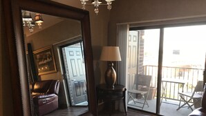 A spacious room with a large mirror, a leather sofa, a small table with a lamp, and a sliding glass door leading to an outdoor area with patio furniture. - Luxury Condo downtown Lansing (Lansing)