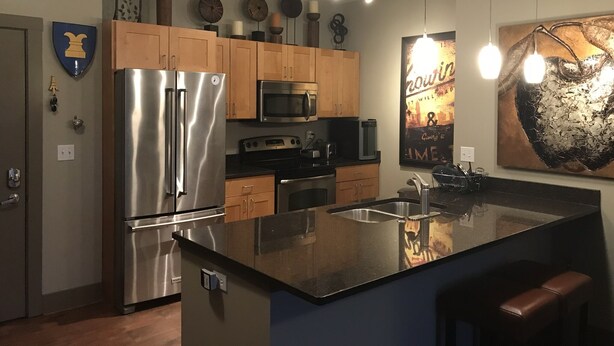 A modern kitchen with stainless steel appliances, wooden cabinets, and a central island. - Luxury Condo downtown Lansing (Lansing)