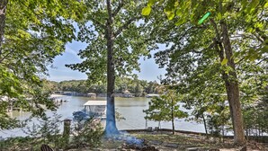 Ett sittområde vid sjön med fyra Adirondack-stolar, en eldstad och utsikt över en sjö med båtar och en brygga i bakgrunden.