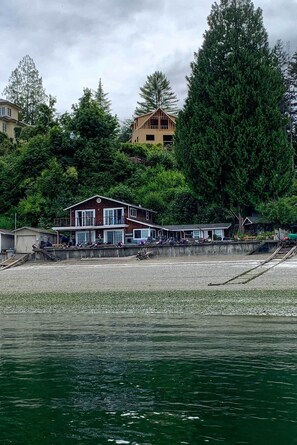Una propiedad frente al agua con una casa grande, un muelle y una construcción pequeña.