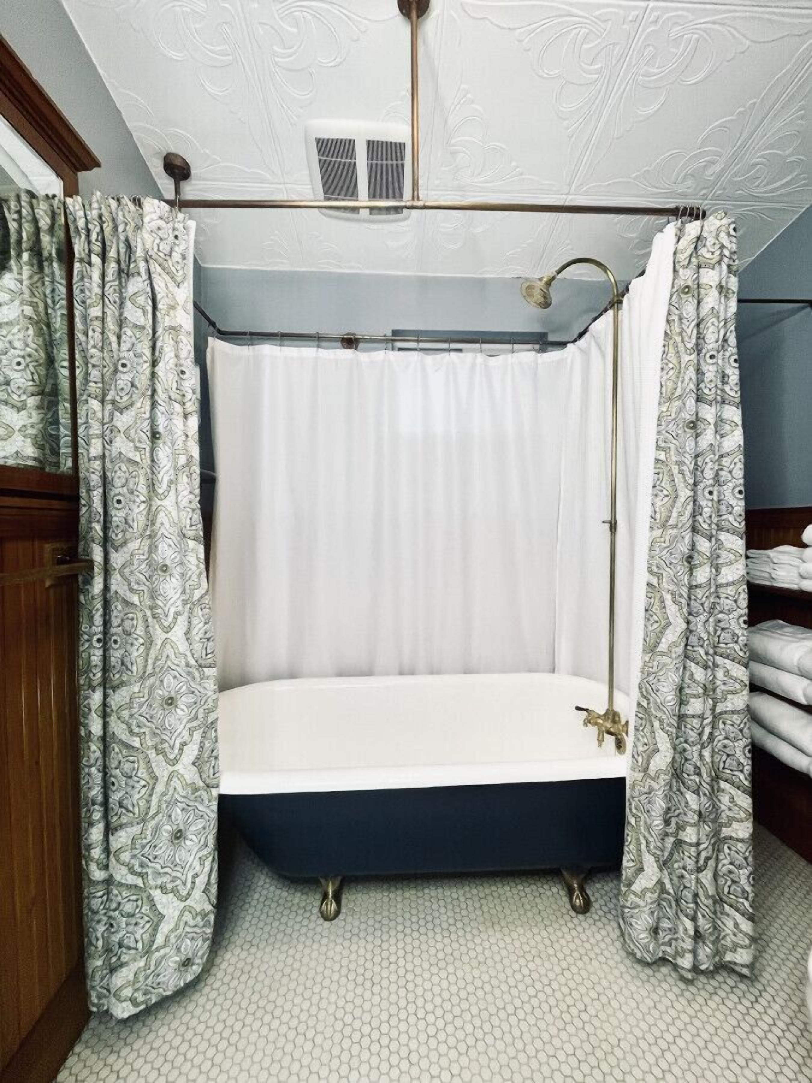 A bathroom with a bathtub, patterned curtains, and a textured ceiling.