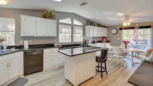 A modern kitchen with white cabinets, a central island, and a dining area with white chairs. - Waterfront Lake Hartwell Home w/ Dock & Fire Pit (Hartwell)