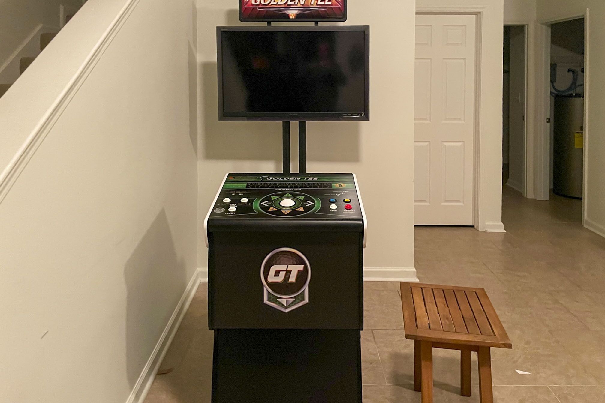 Une console de jeux avec un écran en haut, un logo sur le devant et une petite table en bois à côté.