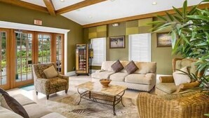 A spacious living area with a sofa set, a coffee table, and a wicker chair. There is a large window with blinds, a plant, and a framed picture on the wall. - Greenlinks Luxury Condo, 3BD, ground floor, golf, pool (Naples)