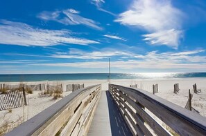 Een houten looppad dat naar een strand leidt, onder een heldere lucht.