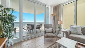 Un balcón con vista a la playa, una silla, una mesa y un sofá.