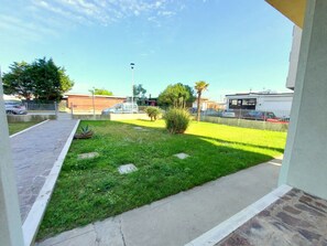A courtyard with a paved walkway, green grass, a palm tree, and a fence.