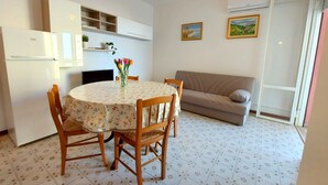 A compact living space with a dining area, a sofa, and a kitchenette. - Cortina 2-9 Two room seafront apartment with air conditioning (Comacchio)