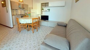 A compact living space with a dining area, kitchenette, sofa, and TV. - Cortina 2-9 Two room seafront apartment with air conditioning (Comacchio)