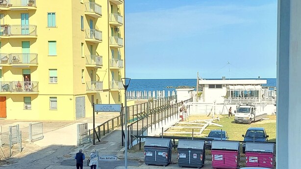 A yellow building with balconies, a street with parked cars, and a view of the sea. - Cortina 2-9 Two room seafront apartment with air conditioning (Comacchio)