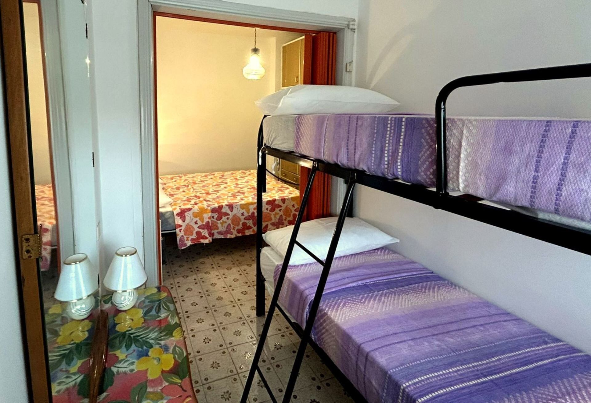 Un dormitorio con literas, una mesita con dos lámparas y una alfombra estampada.