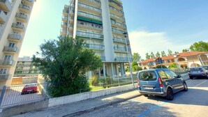 A multi-story residential building with balconies, a parking area with cars, and a clear sky. - Cortina 2-9 Two room seafront apartment with air conditioning (Comacchio)