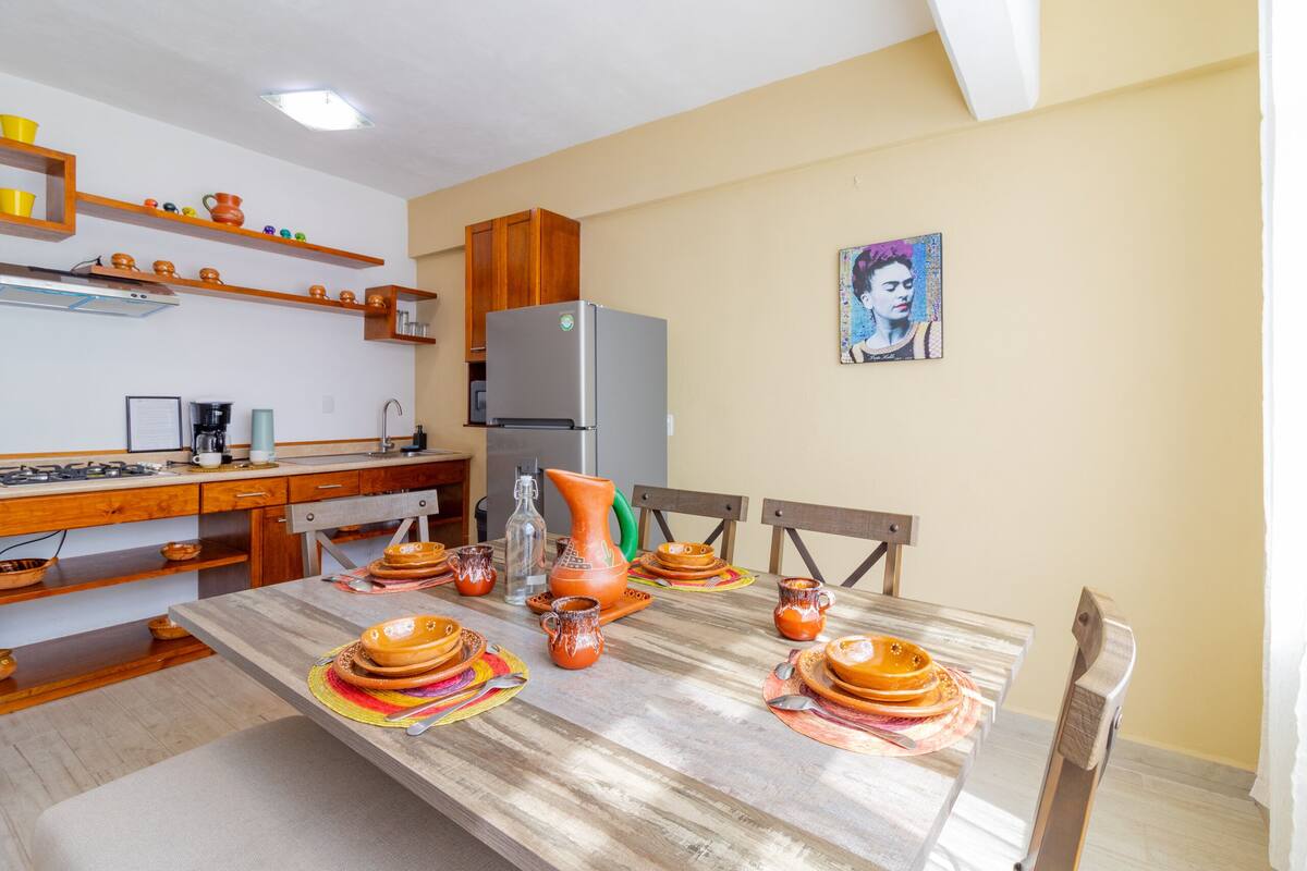 A kitchen with wooden cabinets, a refrigerator, and a dining table set with orange dishes.