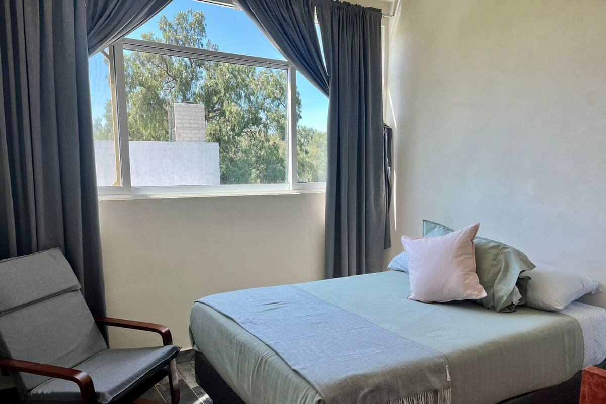 A bedroom with a bed, a chair, and a window with curtains.