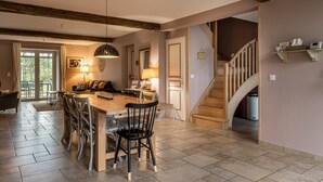 Zona pranzo con tavolo e sedie in legno, un lampadario e una scala che conduce a un altro piano.
