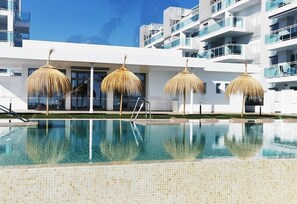 A swimming pool with a tiled edge, surrounded by a white building with balconies and thatched umbrellas. - Apartment "Sunset Duna Beach" with Sea View, Wi-Fi, Balcony & Terrace (Torrox Costa)