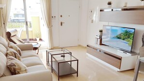 A modern living room with a sofa, a glass coffee table, a flat-screen TV, and a small side table. - Apartment with Large Roof Solarium, Pool, Garden, Barbecue, A/C & Wi-Fi (Orihuela Costa)