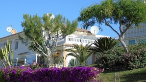 A building with satellite dishes, a balcony, and a garden with purple flowers. - Apartment "Atico Montesol" with Sea View, shared Pool & Terrace (Torrox Costa)