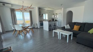 A modern living room with a grey sofa, white coffee table, and dining area with chairs and a table. - Apartment "Atico Montesol" with Sea View, shared Pool & Terrace (Torrox Costa)