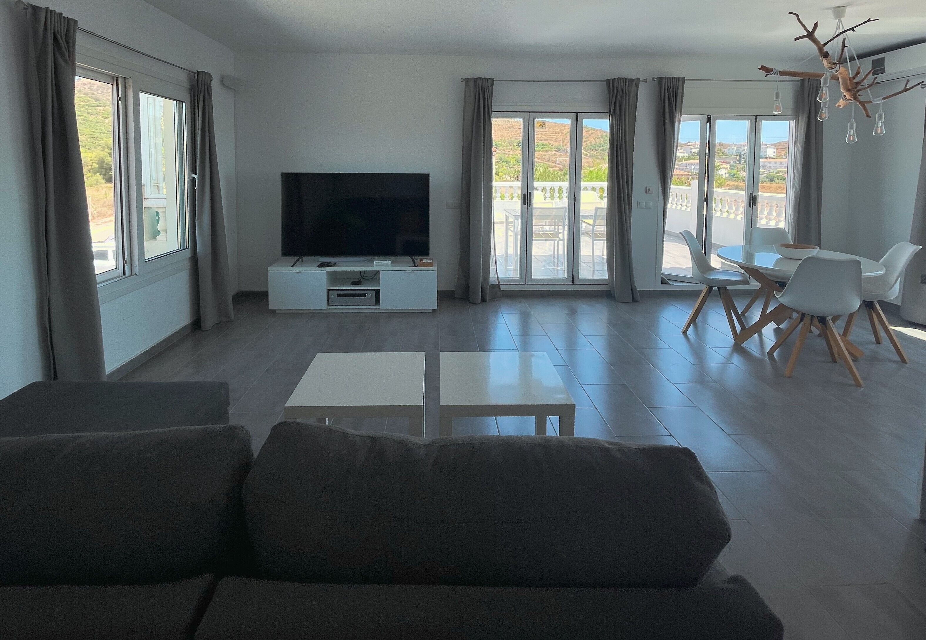 Un salón moderno con televisor de pantalla plana, un sofá, una mesa de comedor con sillas y un balcón con vistas.