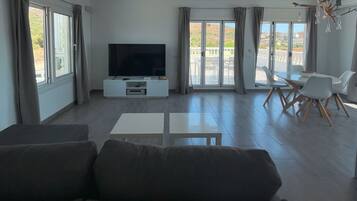 Un salón moderno con televisor de pantalla plana, un sofá, una mesa de comedor con sillas y un balcón con vistas.