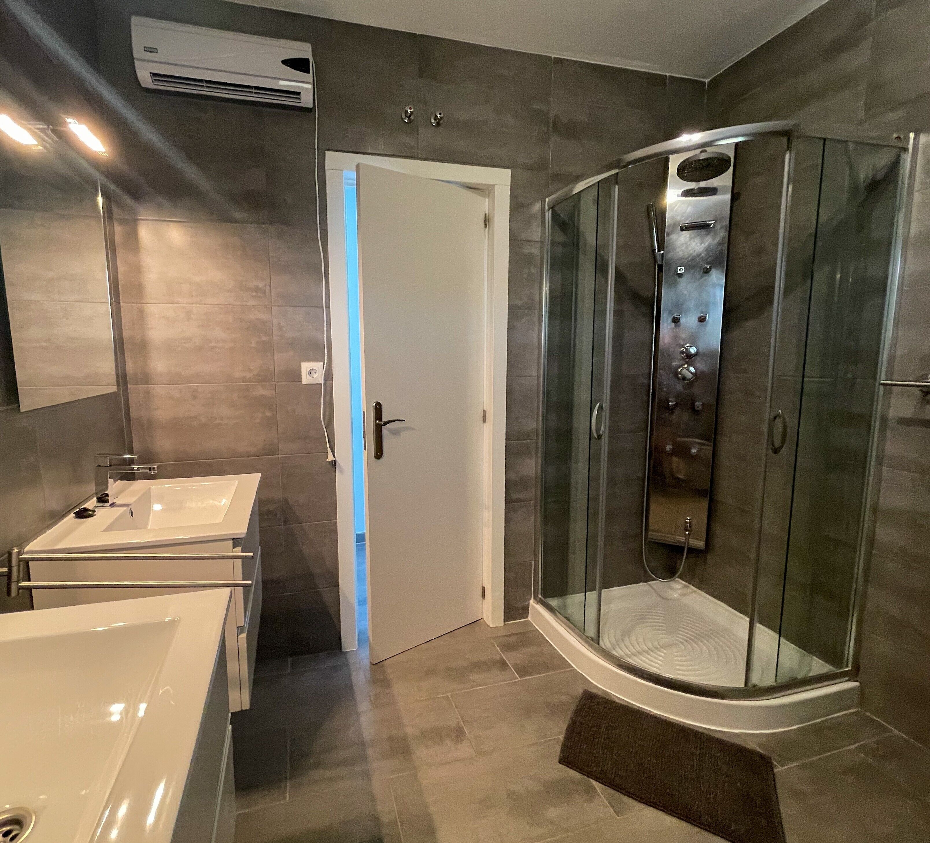 Een moderne badkamer met een douchecabine van glas, een witte badkuip en een wastafel.