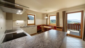 Een moderne keuken met een inbouwfornuis, een zithoek met een bank, en grote ramen met uitzicht op de bergen.