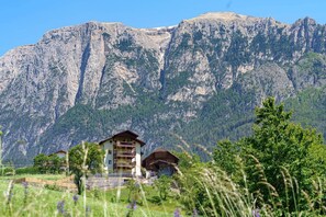 Eine Bergbude mit Balkon, umgeben von üppiger Vegetation und einem felsigen Bergpanorama.