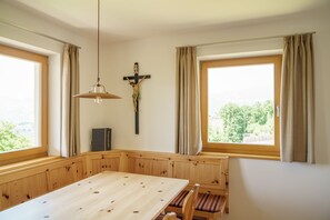 A dining area with a wooden table, benches, a cross, and a view through large windows.
