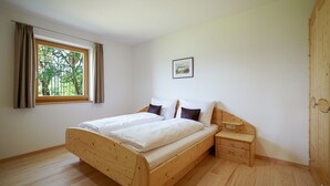Een slaapkamer met een houten bed, nachtkastje, kledingkast en een raam met gordijnen.