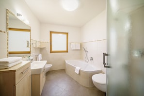 Een badkamer met een bad, toilet, wastafel en spiegel.