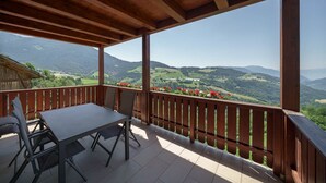 Een houten balkon met een tafel en stoelen, met uitzicht op een bergachtig landschap.