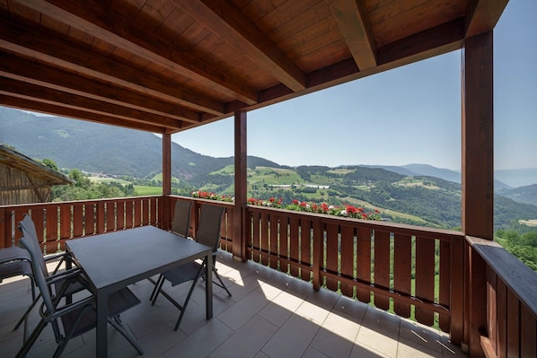 A wooden balcony with a table and chairs, overlooking a mountainous landscape.