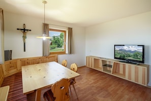 Une pièce comprenant une table à manger en bois, des chaises, un téléviseur et un crucifix au mur.
