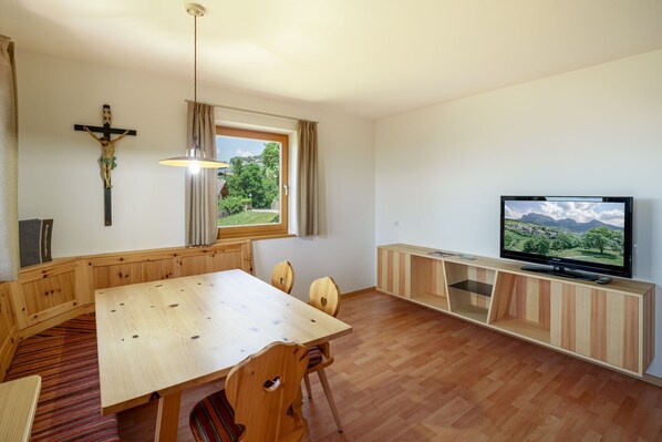 Ein Zimmer mit einem Holzespeisetisch, Stühlen, einem Fernseher und einem Kruzifix an der Wand.