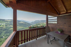 A wooden balcony with a table and chairs, overlooking a mountainous landscape.