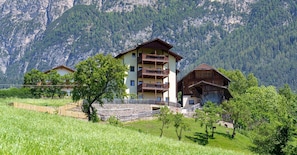 A multi-story building with balconies, surrounded by lush greenery and mountains.