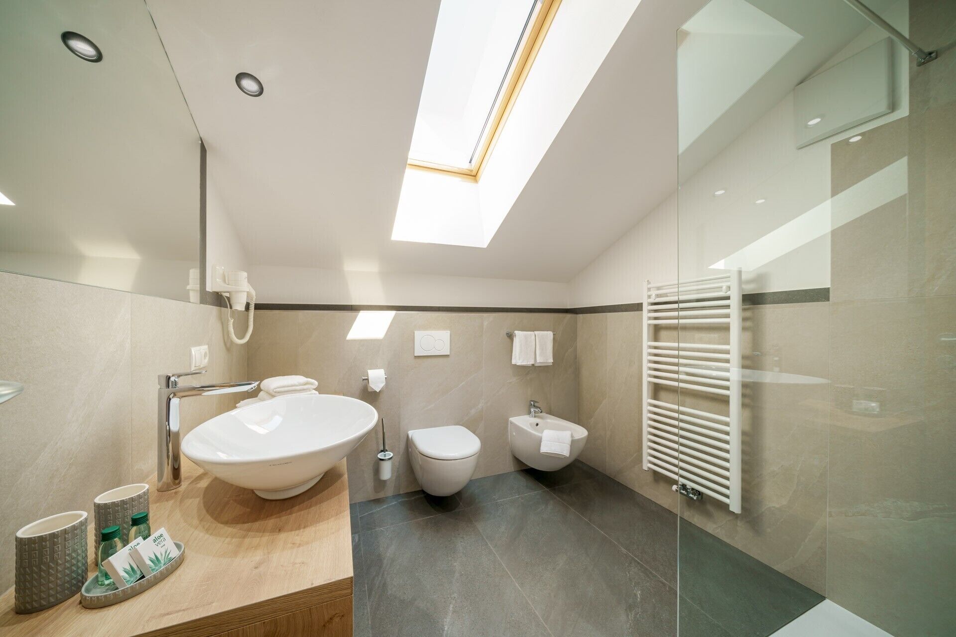 Ein modernes Badezimmer mit Dachfenster, einem großen Waschbecken, einer Toilette und einem Bidet.