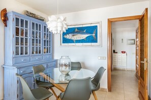 A dining area with a glass table, four chairs, a blue cabinet, and a fish painting on the wall. - Apartment 'Londres 30' with Sea View, Wi-Fi and Air Conditioning (Pollença)